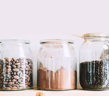 Raw cocoa beans, herbal tea, coffee grains in glass jars on shelves. Organic bulk products in zero waste shop. Foods storage in kitchen at low waste lifestyle. Shopping in plastic free grocery store.の写真素材