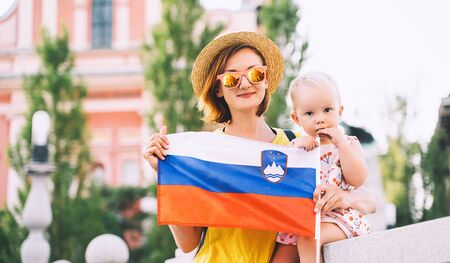Woman with little child holding slovenian flag on central square of Ljubljana. Family walking in european city at spring or summer time. Travel, living, study in Slovenia, Europe.の写真素材