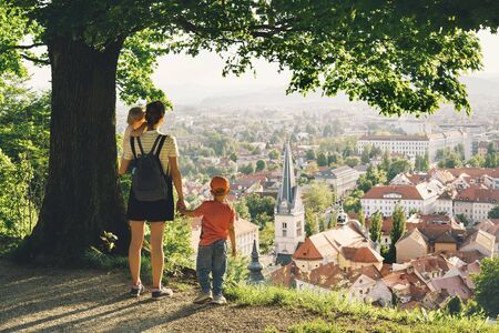 Family on background of Ljubljana, Slovenia, Europe. Woman with two little children looks at panorama of european city from the hill. Mother and kids outdoors at spring or summer time.の写真素材