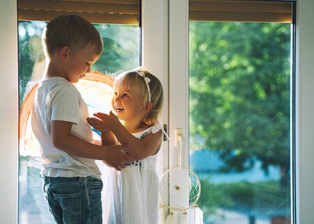 Cute little children on background of painting rainbow on window. Photo of kids leisure at home,...