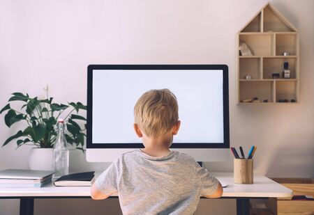 Distance education concept. Kids online learning. Child using computer technology in home schooling. Boy studying on internet with computer with blank white screen at home. Children homeschooling.の写真素材