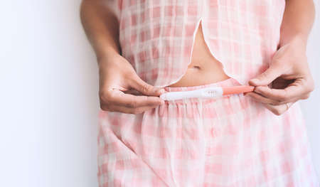 Young woman holding pregnancy test with positive result in hands near her belly. Pregnancy...