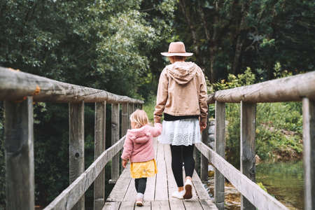 Mother and daughter together on nature. Hikers family outdoor. Woman and little girl are walking on wooden bridge on background with forest. Adventure travel, leisure activities in Slovenia, Europe.の写真素材