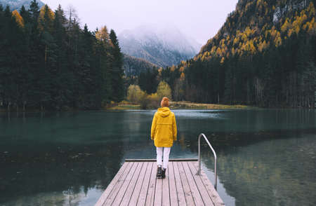 Girl in yellow raincoat looking at mountain lake in Jezersko. Adventure travel in Slovenia. Autumn...