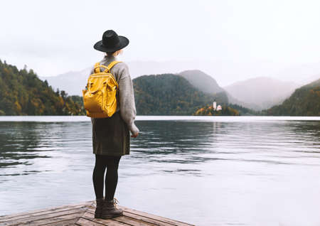 Boho style girl enjoying of beauty autumn in nature near by lake or pond surrounded by branches of willow tree. Woman wearing hat, plaid checkered scarf walking in park or countryside in fall season.の写真素材