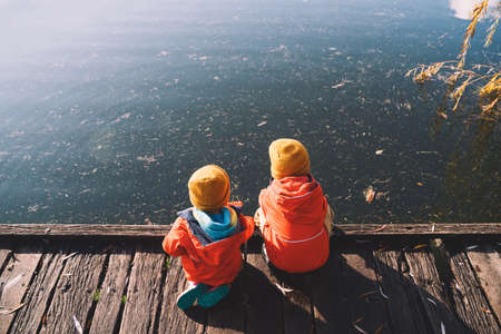 Children spend time outside in fresh and cold air. Small kids play in nature. Healthy childhood. Family life background. Siblings playing near by water in park outdoors. Little friends in countryside.の写真素材