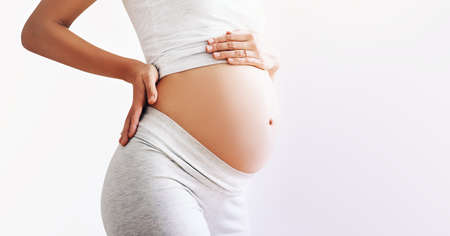 Pregnant woman holds hands on her belly on white background, close-up. Beautiful photo of pregnancy....
