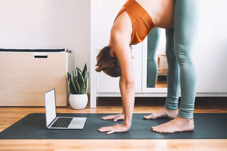 Pregnant woman practicing yoga at home with laptop. Expectant mother doing prenatal video training...