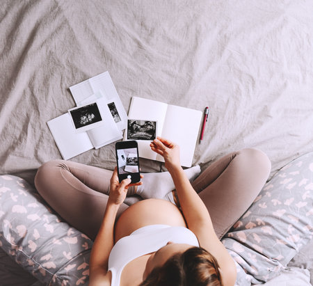 Pregnant woman holding in hands smartphone with empty white display. Close-up pregnant belly of...