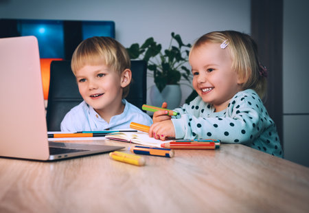School boy and preschool girl with laptop at table in evening at home. Children using digital technology and internet communication. Distance online education or internet entertainment for kids.の写真素材