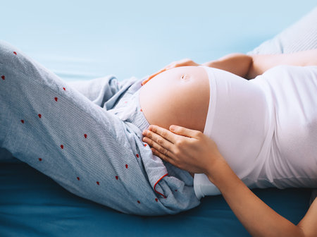 Close-up of beautiful pregnant belly of woman lying in bed. Expectant mother hugging her belly and resting. Loving mother waiting of a baby. Concept of pregnancy, maternity, healthcare, gynecology.の写真素材