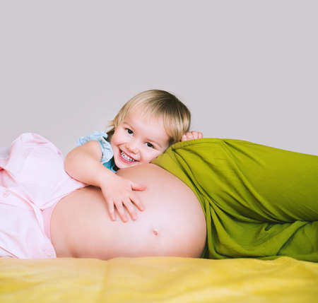 Pregnant mother and daughter together at home. Woman with her first child during second pregnancy. Motherhood and parenting concept. Toddler smiling girl and mom. Happy family expecting for new baby.の写真素材