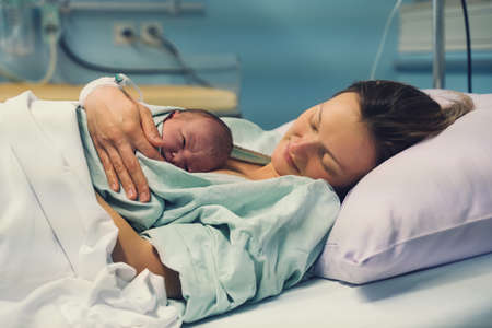 Mother and newborn. Child birth in maternity hospital. Young mom hugging her newborn baby after delivery. Woman giving birth. First moments of baby life after labor.の写真素材