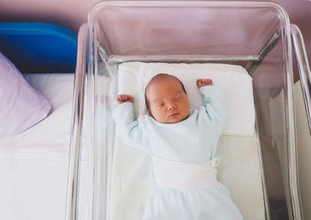 Newborn baby is sleeping in small transparent portable plastic bed. Baby first days of life is lying...