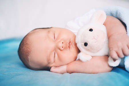 Newborn baby sleep at first days of life. Portrait of new born child boy one week old sleeping peacefully with a cute soft toy in crib in cloth background.の写真素材