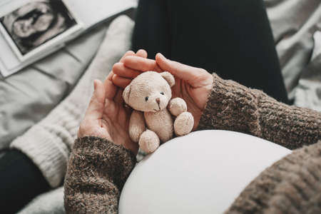Woman pregnant belly with little teddy toy bear. Concept image with symbol of many meanings for expectant mother during pregnancy and her unborn baby.の写真素材