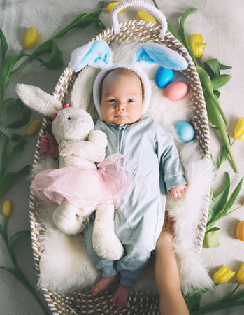 Cute baby Easter bunny. Little baby boy with bunny ears and Easter eggs in wicker basket in white fur. Symbol of Easter holiday, birth, spring, religion.の写真素材