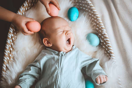 Cute baby Easter bunny. Little baby boy with bunny ears and Easter eggs in wicker basket in white...