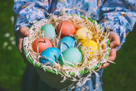 Colorful Easter eggs in basket. Children gathering painted decoration eggs in spring park. Kids hunt...