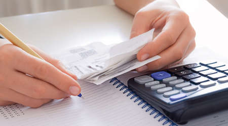 woman hands holding pen and checks and using calculator for calculations on desk at home office.