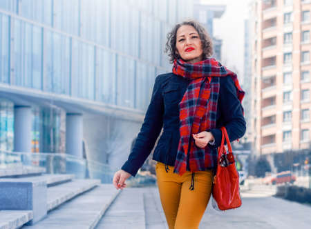 Business woman in a red scarf with a red bag stands on the steps near the business center.の写真素材