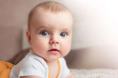 Portrait of a baby girl with big blue eyes lying on her stomach on the bed and looking at the camera.の写真素材