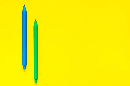 Blue and green color pens isolated on yellow background. Minimalist flat lay. Copyspace. Concept work and education. Office school supplies. Closeup view.の写真素材