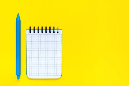 Blue pen and open notepad isolated on yellow background. School and office supplies. Concept of back to school and education. Minimalist flat lay. Empty place for writing. With copy space.の写真素材