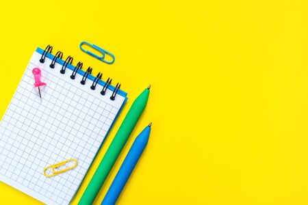 School and office supplies on yellow background. Blue and green pens and open notepad with blank sheet. Concept of back to school and education. Minimalist design. Flat lay. With copy space.の写真素材