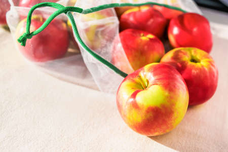 Fresh ripe apples in reusable eco-friendly mesh bag lie on the table. Sunny day. Plastic free, zero waste and sustainable lifestyle concept. Reusable using. Environmental concern. Closeup view.の写真素材