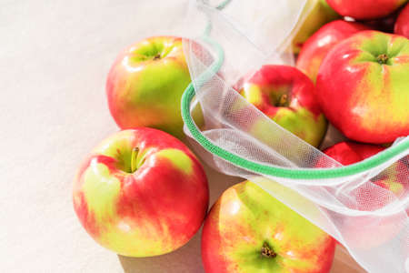 Fresh ripe and juicy apples in reusable eco-friendly mesh bag lie on the table. Sunny day. Plastic free, zero waste and sustainable lifestyle concept. Reusable using. Closeup view.の写真素材