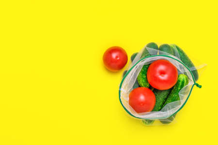 Fresh ripe and juicy vegetables in reusable eco-friendly mesh bag on the yellow background. Plastic free, zero waste, and sustainable living concept. Reusable using. Copy space.の写真素材