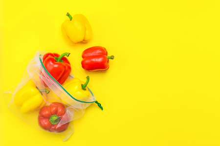 Fresh ripe red and yellow peppers in reusable eco-friendly mesh bag on the yellow background. Plastic free, zero waste, and sustainable living concept. Reusable using. Closeup view. Copy space.の写真素材