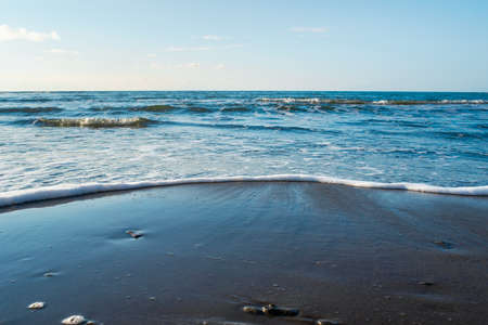 Wild beach of the Sea of Okhotsk, Sakhalin island, Russia. Beautiful seascape. Endless sea and clear blue sky. Waves are washed up to the shore. Beauty in nature. Natural background with copy space.の写真素材