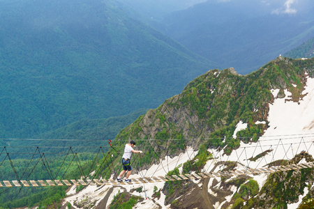 Estosadok, Sochi, Russia - June 10.2017: tourist goes on a rope bridge stretched over the gorge to the ski resort "Rosa Khutor". Cloudy summer dayのeditorial素材