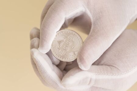 Hands in white gloves carefully hold a silver coin bitcoin. Hope for capital growthの写真素材