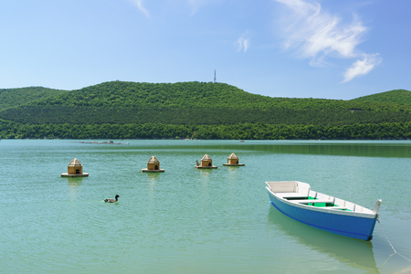 Bright blue empty rowing boat and duck houses on the green water of the mountain lake Abrau-Durso. Sunny day to relax in the fresh airの写真素材