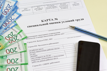 Form in Russian: "Map of special assessment of working conditions", smartphone, ballpoint pen and new Russian rubles on the table. Summing up the results of the special assessmentの写真素材