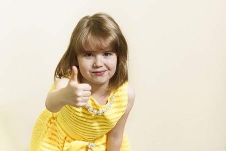 A little beautiful girl in a yellow dress shows her thumb. That is all right. It worked. Ok