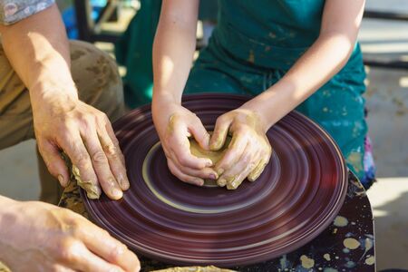 Master and student. Childrens hands in the yellow clay on the rotating Potters wheel molded the dishes. Craftの写真素材