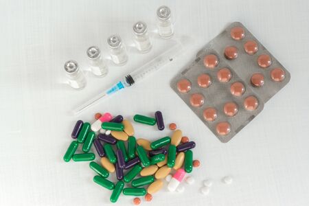Tablets and capsules, a syringe and vials of medicine on a white table. Pharmaceuticals for the...
