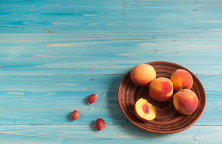 Four whole and sliced fresh juicy peaches lie on a clay plate on a wooden table. Copy spaceの写真素材