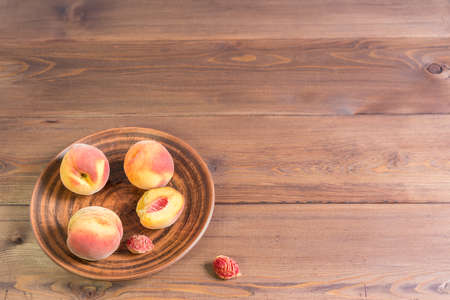 Four ripe velvety peaches on an earthenware platter and the seeds are laid on a natural brown wooden table. Sunny summerの写真素材