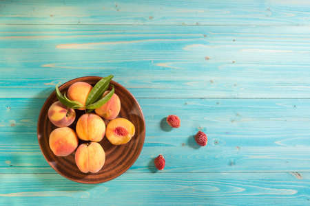 Several ripe velvety juicy and beautiful peaches with leaves lie in a plate on a blue wooden table. Sunny summer. The view from the top. Copy spaceの写真素材
