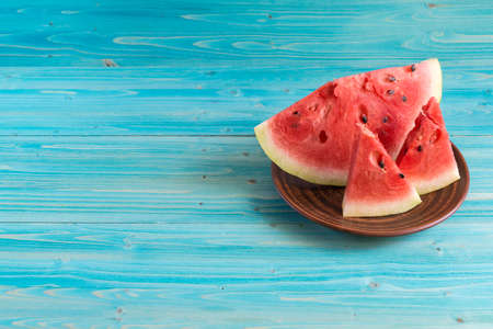 Three slices of ripe fresh watermelon lie in a clay plate on a blue wooden table. Copy spaceの写真素材
