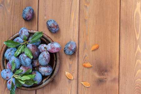 A few washed ripe blue plums in a brown dish on the wooden table. Several bones lie separately. Copy...