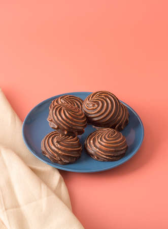 Traditional Russian vanilla marshmallow in chocolate glaze in a blue plate on a pink background....