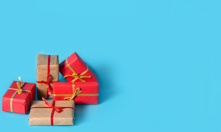 A lot of boxes with gifts in red and natural paper with gold and red ribbons on a light blue...
