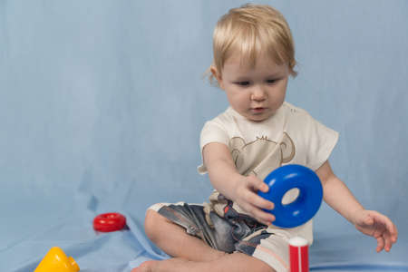 A small blonde child sits on a blue background and plays with toys