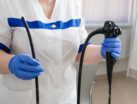 A female doctor in a white suit holds medical equipment for video esophagogastroduodenoscopy in her...